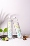 Two bottles of Botanica herbal water on a white background with herbs and spices.
